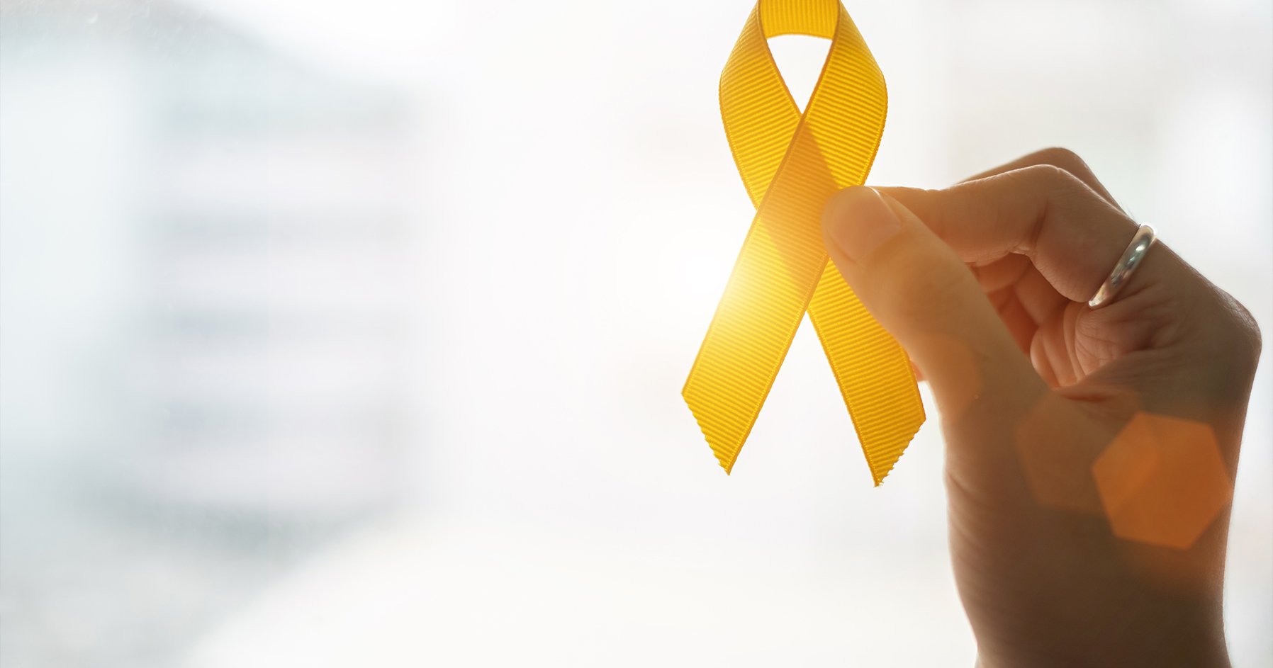 Image of a hand holding a yellow ribbon representing cancer survivors. 